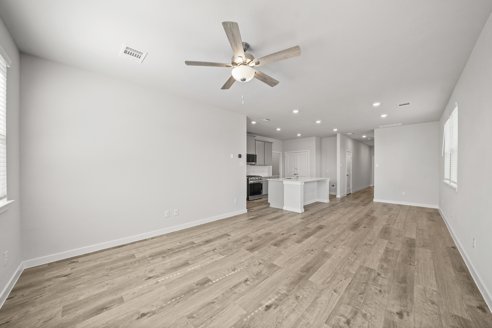 A large empty room with a ceiling fan and a wood floor.
